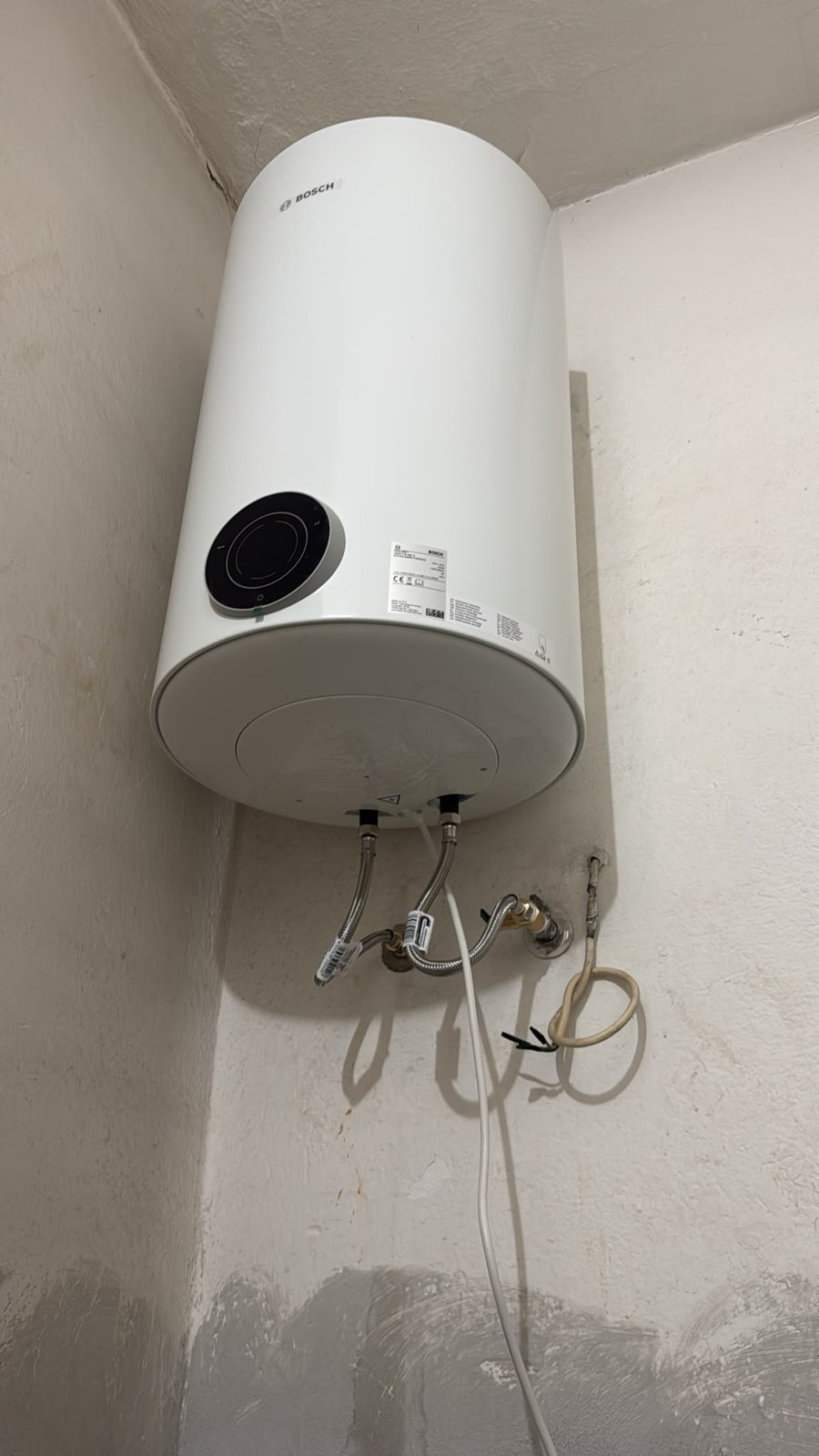 Scaldabagno elettrico Bosch bianco fissato nell'angolo, con tubi flessibili e cavo sotto